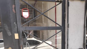 Une porte en métal noir avec un panneau de verre, un cadenas et une enseigne rouge et blanche fixée sur le cadre de la porte.