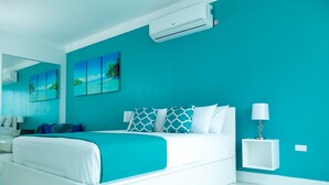 A modern bedroom with a large bed, a nightstand, a wall-mounted air conditioner, and a painting of a beach scene. - 20 South Apartments (Kingston)