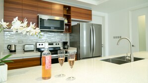 A modern kitchen with wooden cabinets, stainless steel appliances, a microwave, a refrigerator, a sink, and two glasses of wine on the counter. - 20 South Apartments (Kingston)