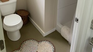Et badeværelse med toilet, brusebad og en lille måtte på gulvet.