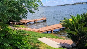 Vista sul lago con moli di legno che si protendono nell'acqua, circondate da vegetazione lussureggiante e piante fiorite.