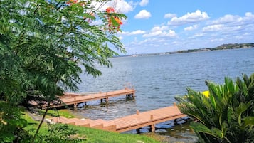 A lakeside view with wooden docks extending into the water, surrounded by lush greenery and flowering plants.