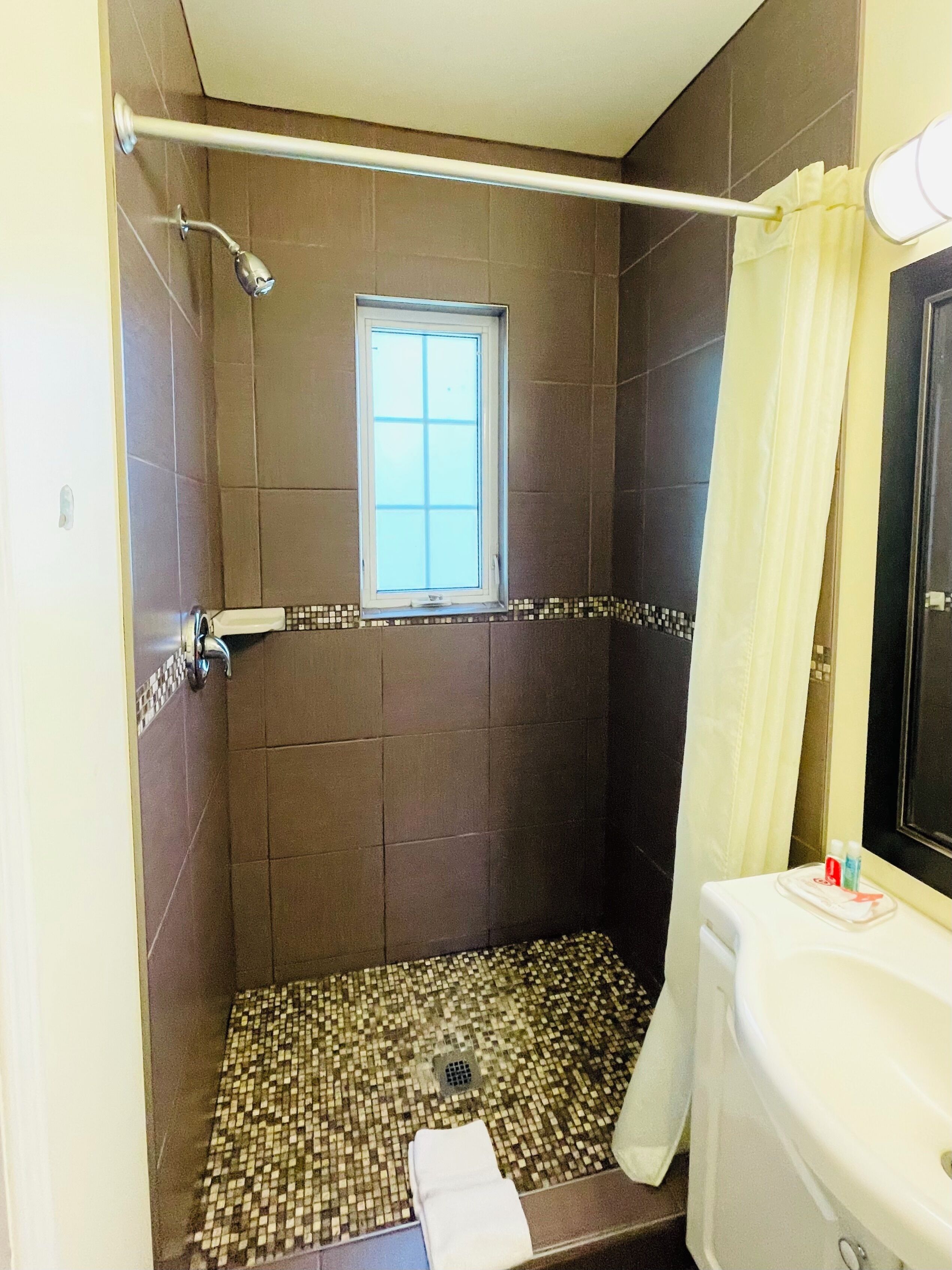 A shower with a tiled floor, a window, and a toilet with a mirror.