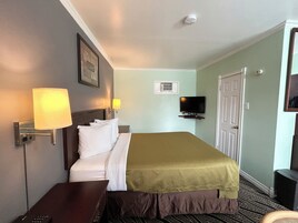 Habitación de hotel con cama, lámparas de noche, televisión, aire acondicionado y una puerta.