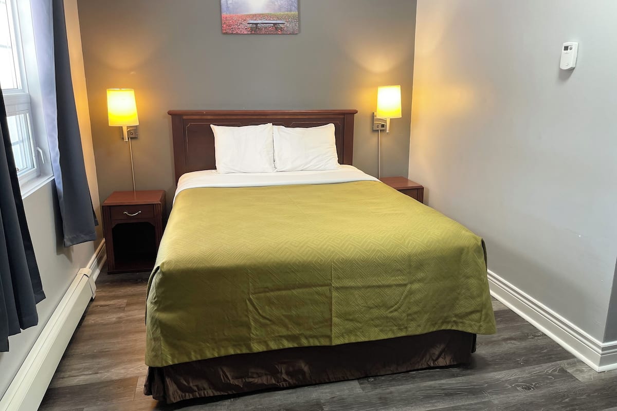 A neatly made bed with a green bedspread, two bedside lamps, a nightstand, and a framed picture on the wall.
