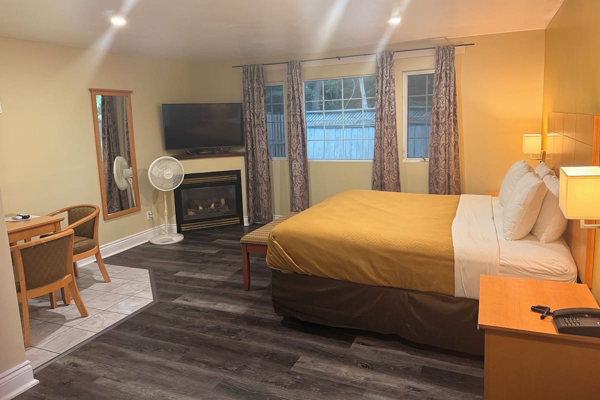 A hotel room with a bed, a desk with a chair, a television, a fireplace, and a window with curtains.