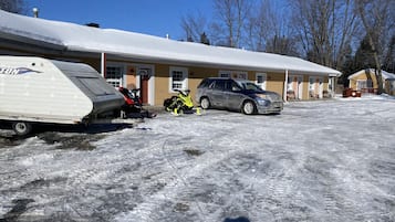 Um motel com uma caravana estacionada na frente, chão coberto de neve e um SUV estacionado.