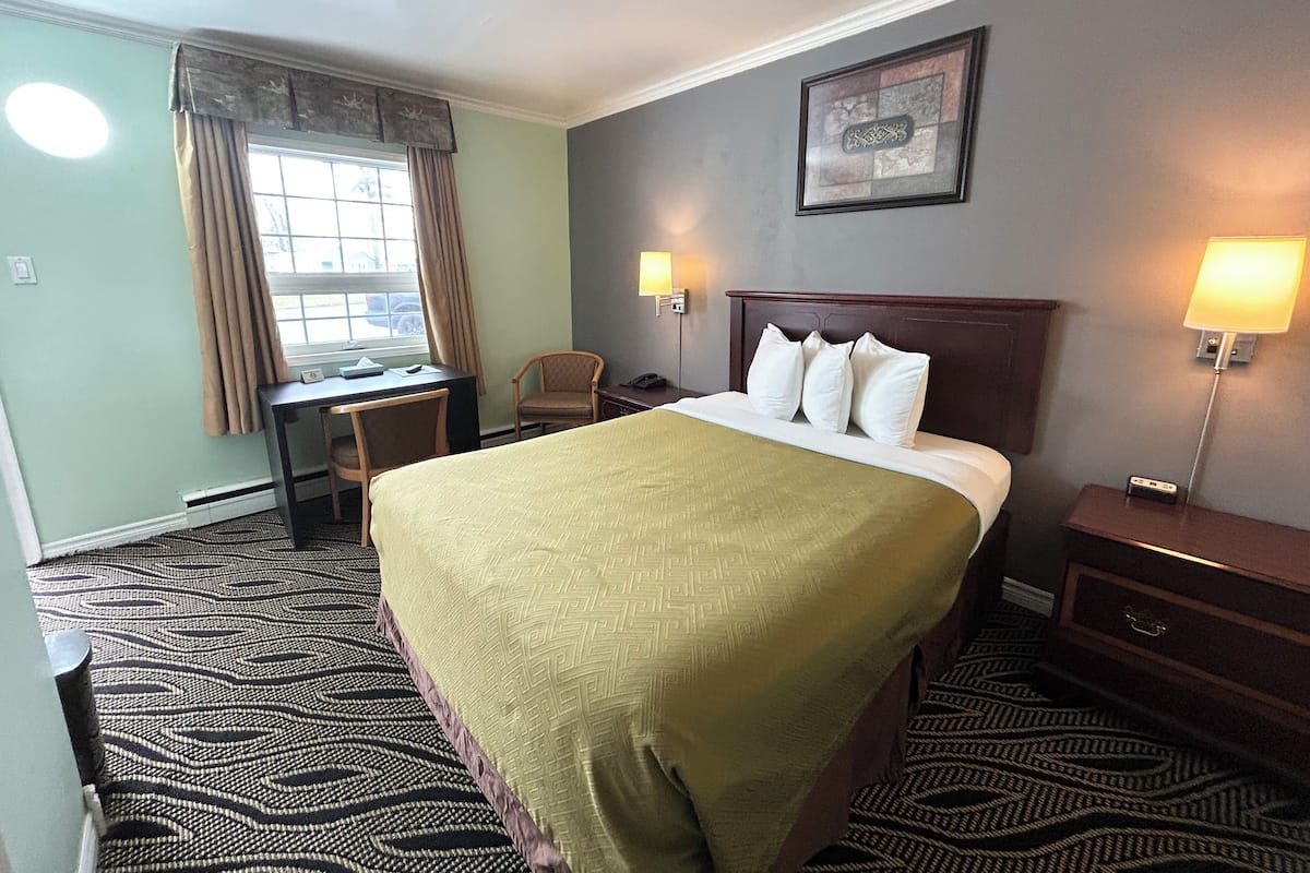 A hotel room with a large bed, a desk, a chair, a nightstand, and a window with curtains.