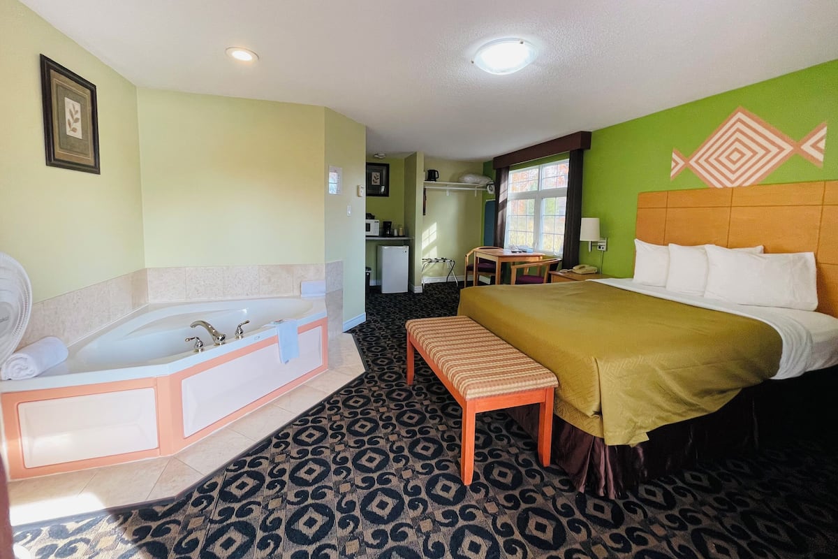A hotel room with a large bed, a separate bathroom with a bathtub, a small table, and a chair.