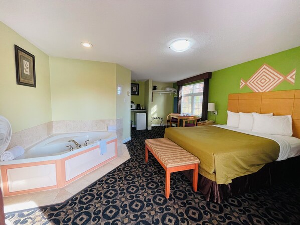 A hotel room with a large bed, a separate bathroom with a bathtub, a small table, and a chair. - North Bay Inn (North Bay)
