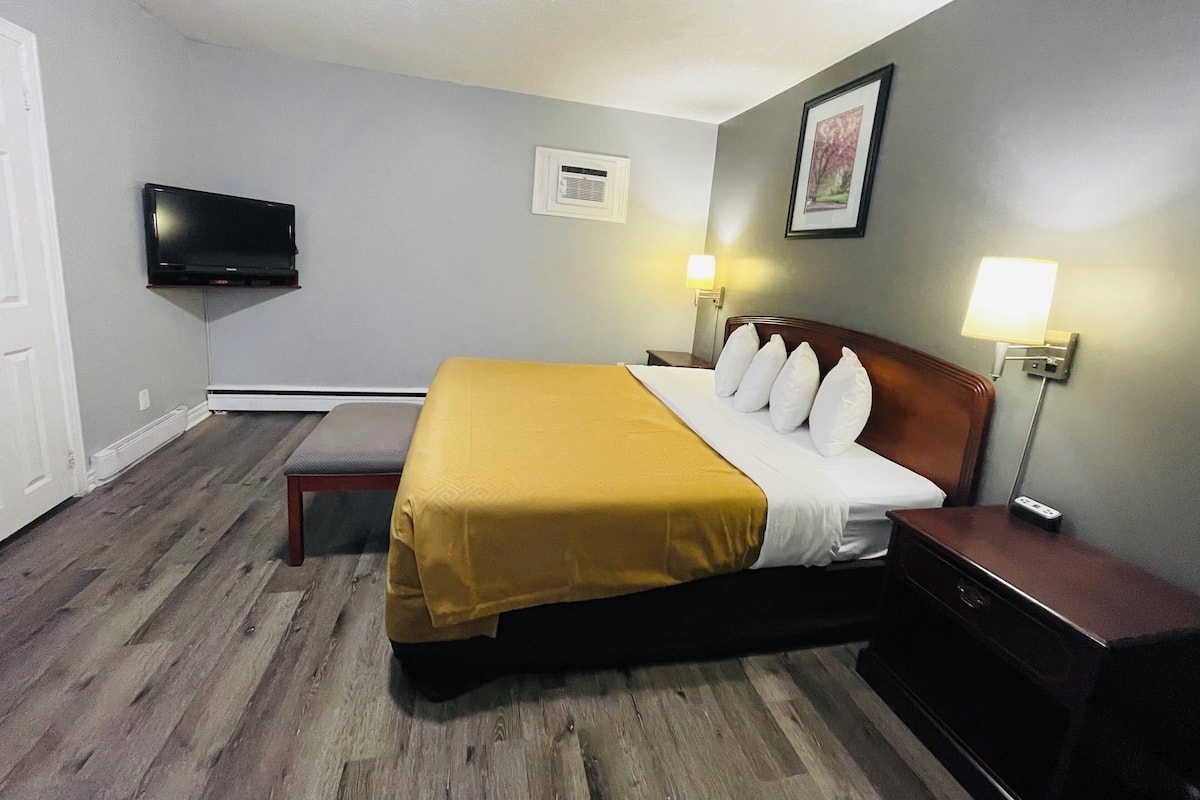 A hotel room with a bed, bedside tables, a television, and a wall-mounted air conditioning unit.