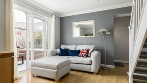 Un salon moderne avec un canapé gris, un pouf blanc et une lampe sur pied.