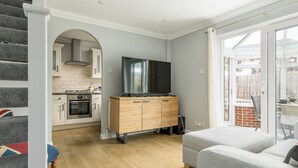 Une cuisine moderne dotée d’un four et d’un micro-ondes encastrés, d’un meuble en bois avec un téléviseur à écran plat, et d’une porte-fenêtre coulissante donnant sur un balcon avec un mur en briques.