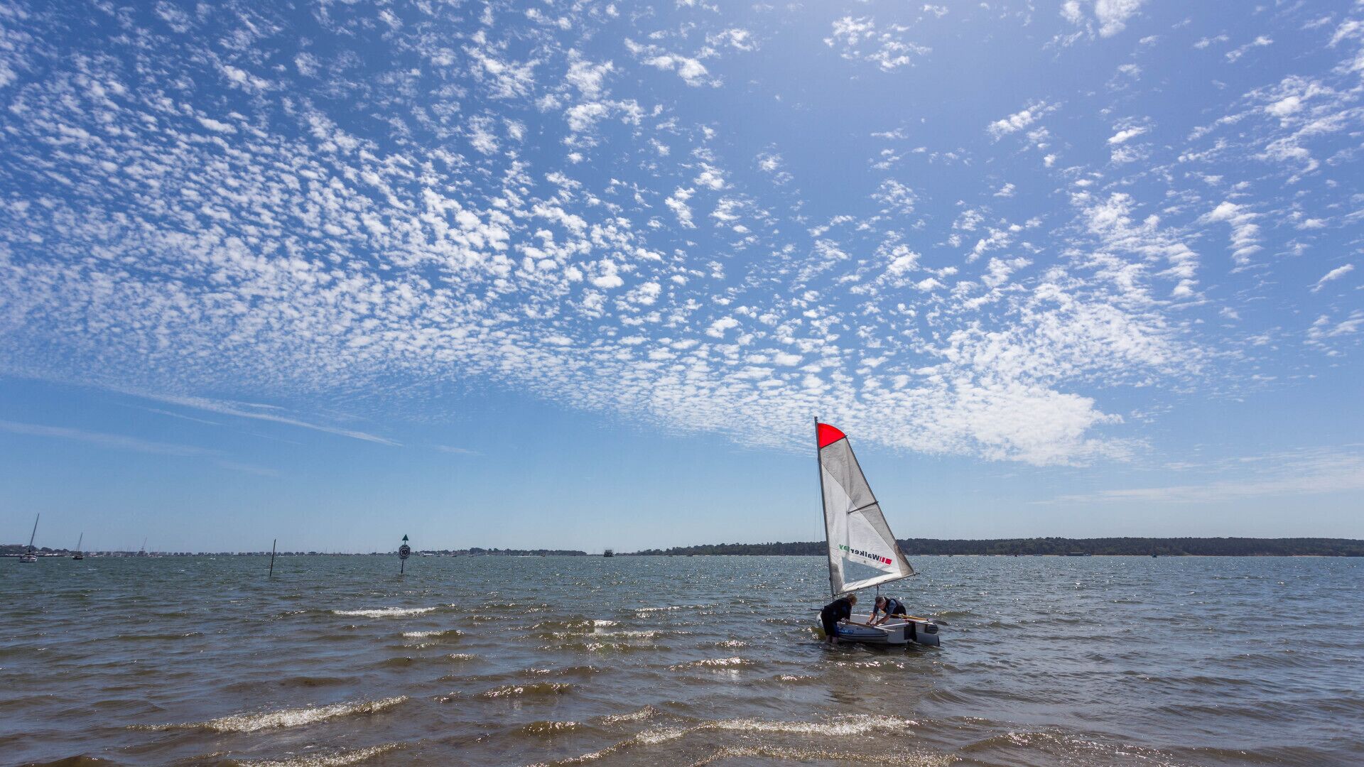 Un velero en aguas tranquilas bajo un cielo despejado con algunas nubes dispersas.