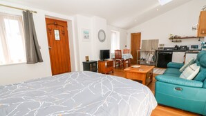 Une chambre avec un grand lit, un canapé de couleur turquoise, une table à manger en bois et, au fond, un coin cuisine.