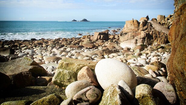 Une plage rocheuse parsemée de gros rochers, offrant une vue dégagée sur l’océan.