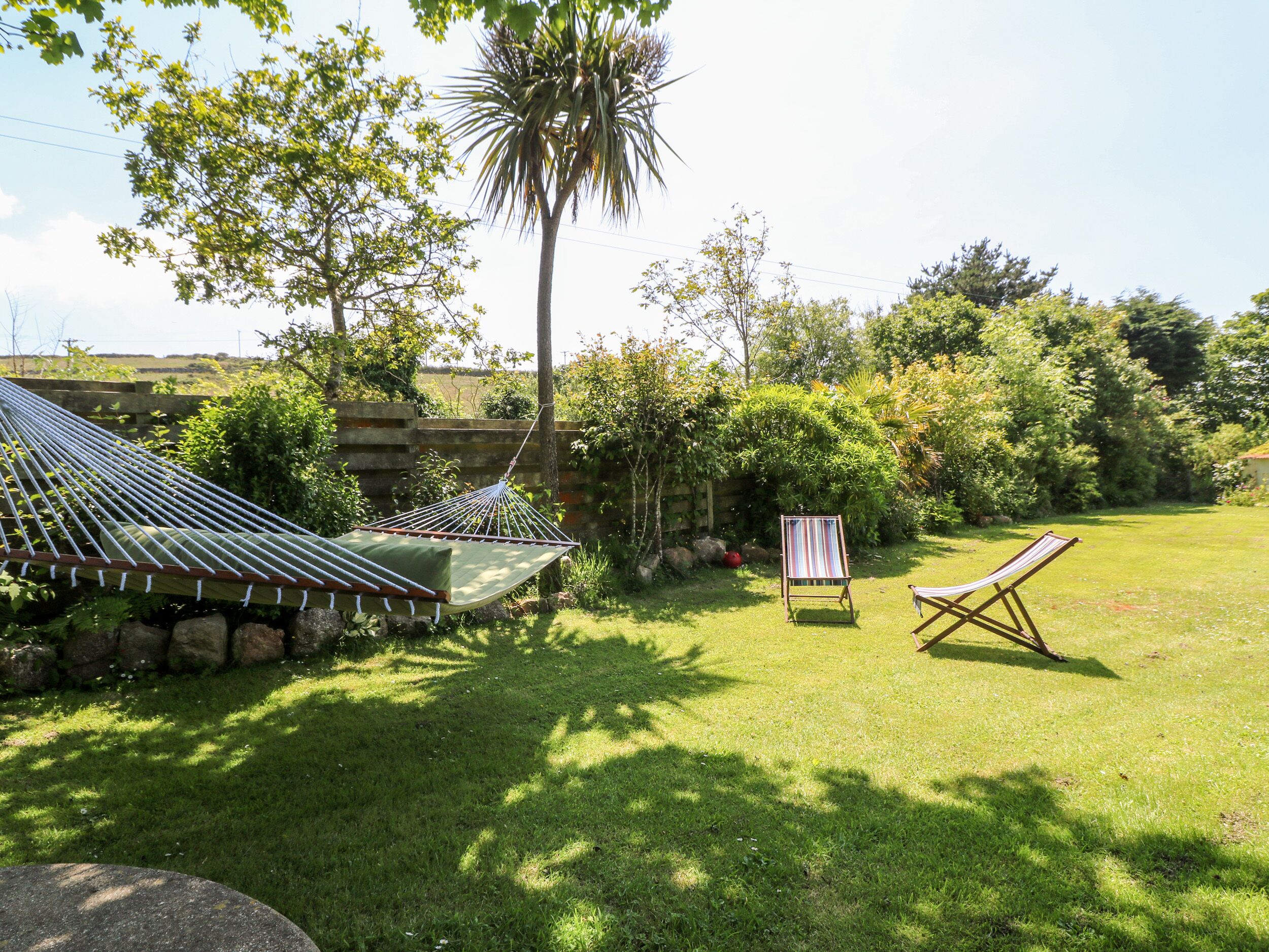 A hammock, two striped chairs, and a stone wall in a lush garden.