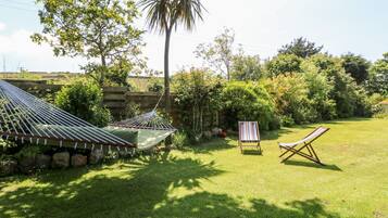 A hammock, two striped chairs, and a stone wall in a lush garden.