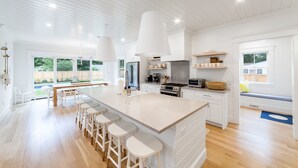 Una cocina moderna con una isla grande, taburetes de bar y vista al jardín trasero.