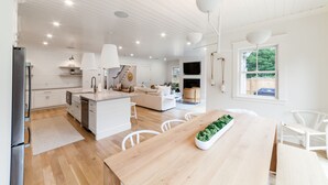 Una cocina moderna con armarios blancos, una isla central y una zona de comedor con mesa y sillas de madera.