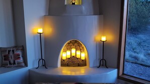 A cozy room with a fireplace, two candles, a table with magazines, and a window with a view of trees. - Dark Sky Retreat Near Santa Fe (Santa Fe)
