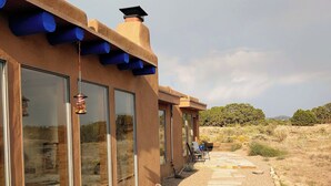 A modern building with large windows, a stone pathway, and a desert landscape in the background. - Dark Sky Retreat Near Santa Fe (Santa Fe)