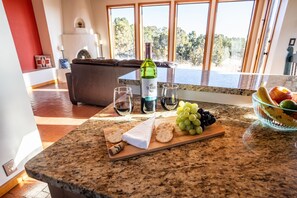 Una encimera de cocina con una botella de vino, copas, queso, uvas y un bol de fruta.