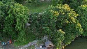 Une maison entourée d’une forêt dense, avec un petit quai et un espace extérieur aménagé pour s’asseoir.