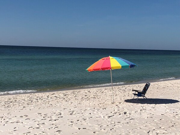 A beach with a colorful umbrella and a chair.