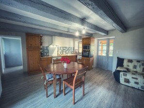 A spacious kitchen with wooden cabinets, a dining table with chairs, and a built-in microwave. - Maisonnette Campagne Dordogne (Coursac)