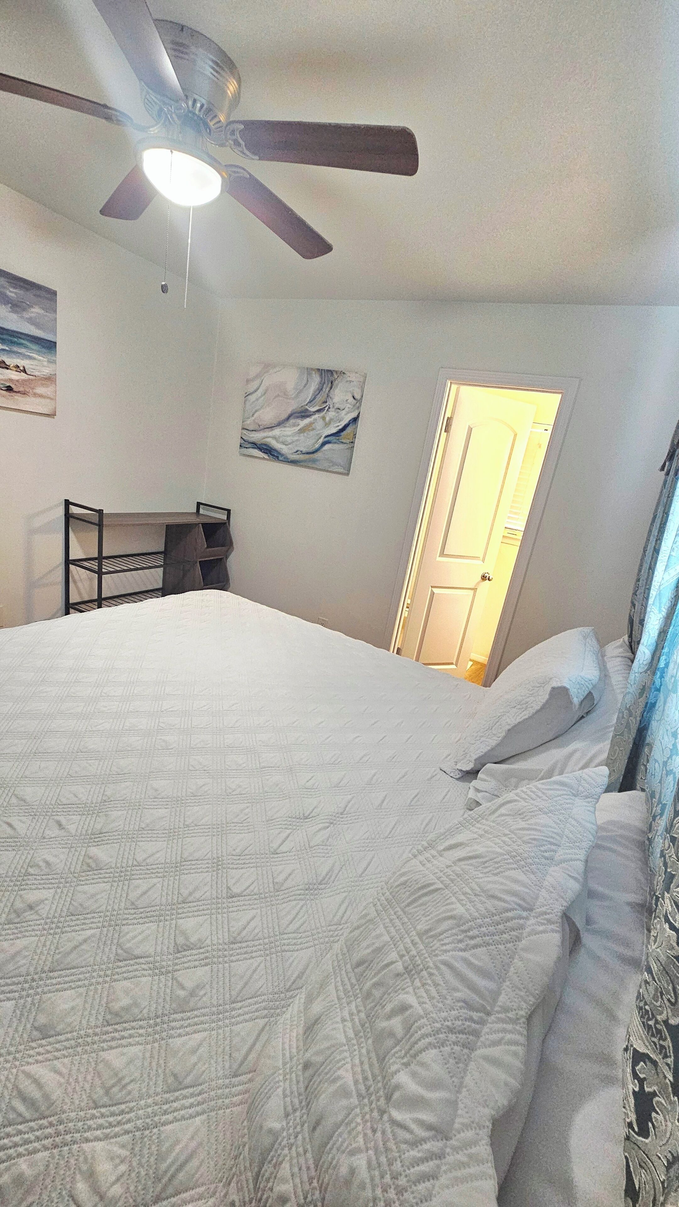Een slaapkamer met een bed, een plafondventilator, een schilderij en een deur.