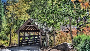 Ein hölzerner Pavillon mit geneigtem Dach, umgeben von Bäumen und einem Kiesweg.