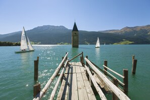 A wooden pier extending into a lake with sailboats and a tower in the background.