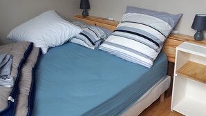 Ein ordentlich bezogenes Bett mit blau-weißer Bettwäsche, ein Nachttisch aus Holz mit einer Lampe und ein weißer Beistelltisch.