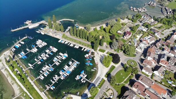 An aerial view of a marina with numerous boats docked, surrounded by residential buildings and greenery. - Small 3-room apartment with large terrace, 150m to the lake (Uhldingen-Mühlhofen)