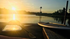A wooden dock with a paddle and a kayak, overlooking a calm body of water with a windmill in the distance. - Cozy Rustic Cabins for Self or Family Retreat (Whitewright)