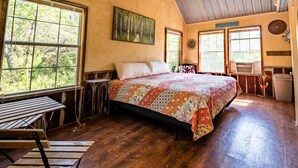A rustic bedroom with a large bed, wooden flooring, and large windows offering a view of the outdoors. - Cozy Rustic Cabins for Self or Family Retreat (Whitewright)