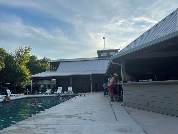 Un área de piscina con sillas de descanso, una zona de estar cubierta y un edificio con techo de metal.