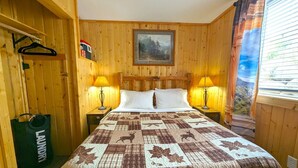 Una stanza accogliente in legno con un letto, due lampade da comodino, un quadro appeso e una finestra con tende.
