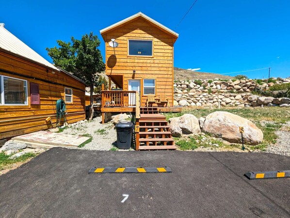 A wooden cabin with a deck, a satellite dish, and a paved area with numbered parking spaces. - Yellowstone's Treasure Cabin #7, few min drive to Yellowstone's North Entrance (Gardiner)