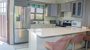 A modern kitchen with a central island, stainless steel appliances, and bar stools. - Water Mills Beach Apartments (Ocho Rios)