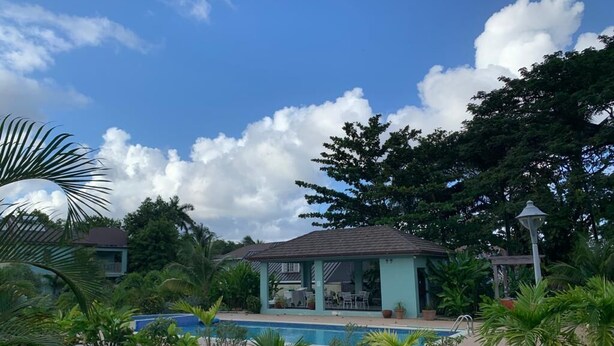 A pool area with a covered seating area, surrounded by tropical plants and trees. - Water Mills Beach Apartments (Ocho Rios)