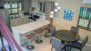 A modern kitchen with a central island, bar stools, and a dining table with chairs. - Water Mills Beach Apartments (Ocho Rios)
