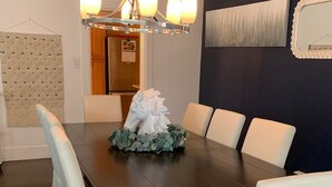 Une salle à manger avec une table en bois foncé, entourée de chaises à revêtement blanc, un lustre et une statue équestre décorative qui sert de centre de table.