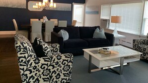 Un salon avec un mur d’accent bleu foncé, un lustre, une table basse blanche et des fauteuils à motifs.