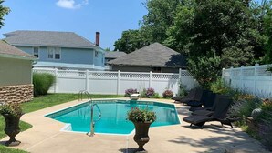 Un jardin avec une piscine, une clôture blanche et un espace patio aménagé avec des chaises longues.