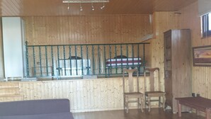 Een ruime woonkamer met houten vloer, een bank, een eettafel en een keuken met een koelkast en een spoelbak.