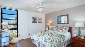 Ein Schlafzimmer mit einem großen Bett, einem Deckenventilator, einem Fenster mit Blick auf die Stadt, einem Sessel und einem Nachttisch.