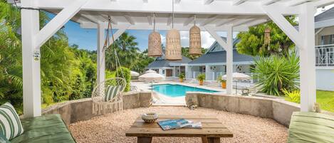 A covered outdoor seating area with a pool in the background.