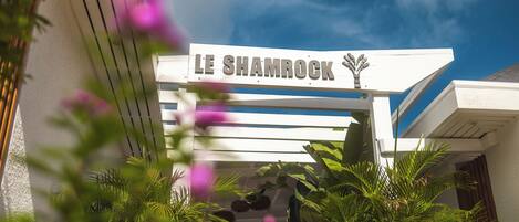 The exterior of Le Shamrock with a clear sky and lush greenery.